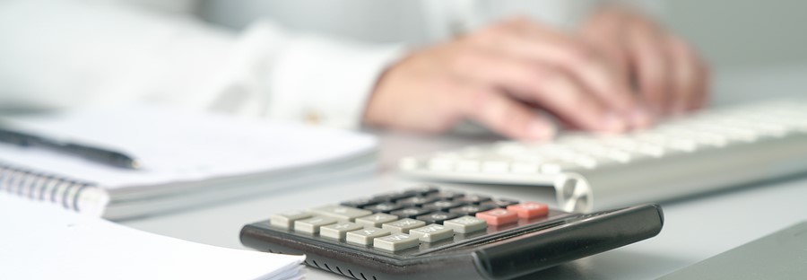 Office table view with Accountant or Professional woman Executive working out of focus. Focus on calculator.