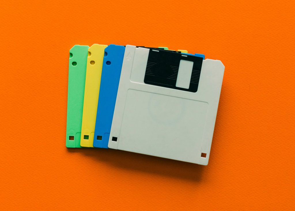 A fanned-out stack of multicolor floppy disks lying flat on a bright orange surface.