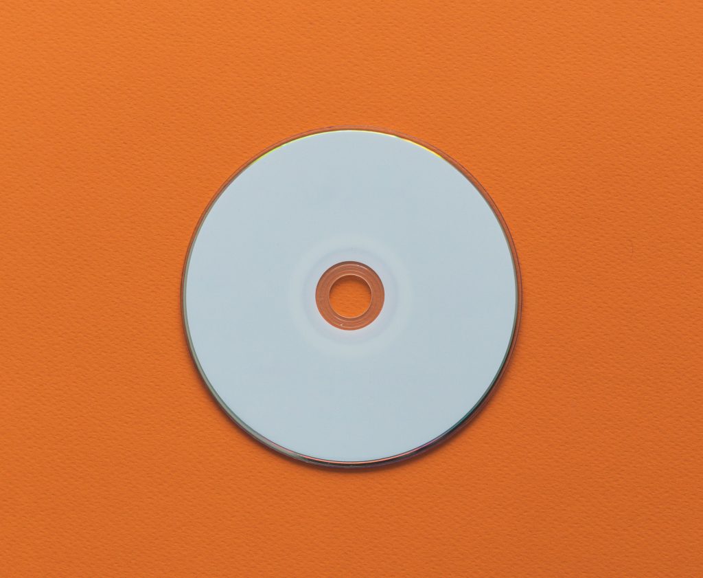A plain white compact disc (CD) lying flat on a bright orange surface.
