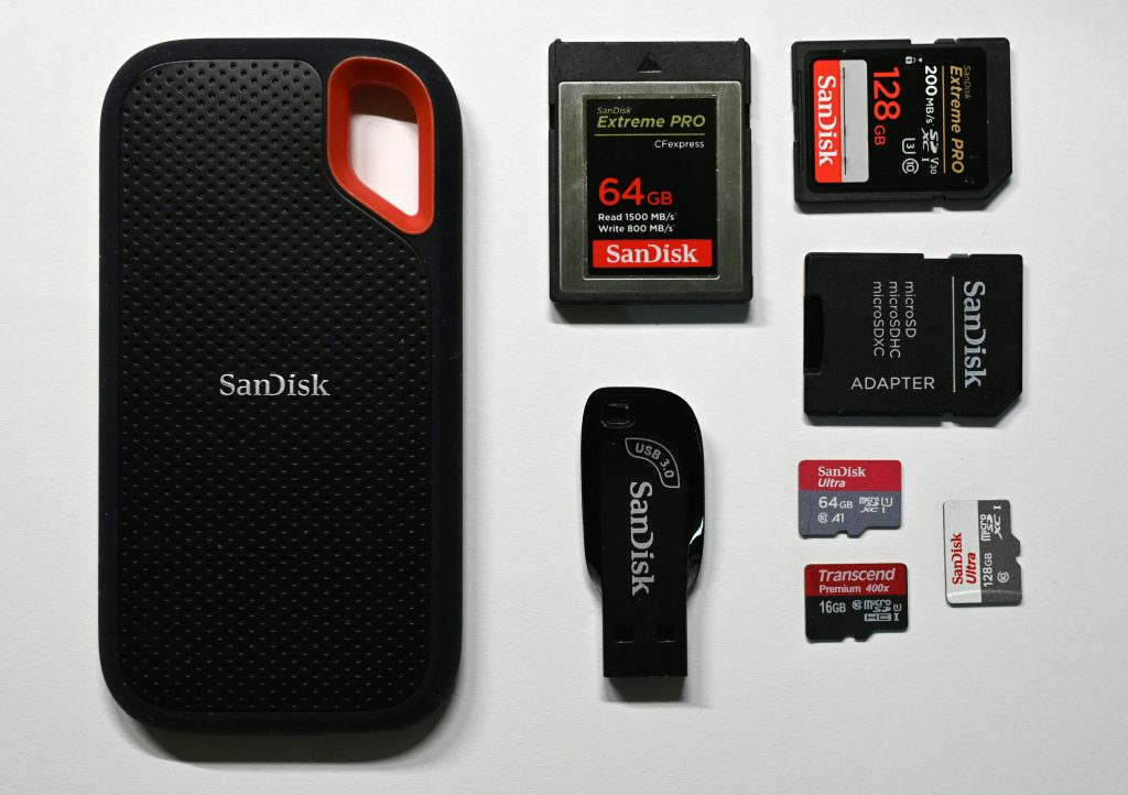 Black storage devices with red accents on a white surface, including USB flash drives, SD cards, and an external hard drive.